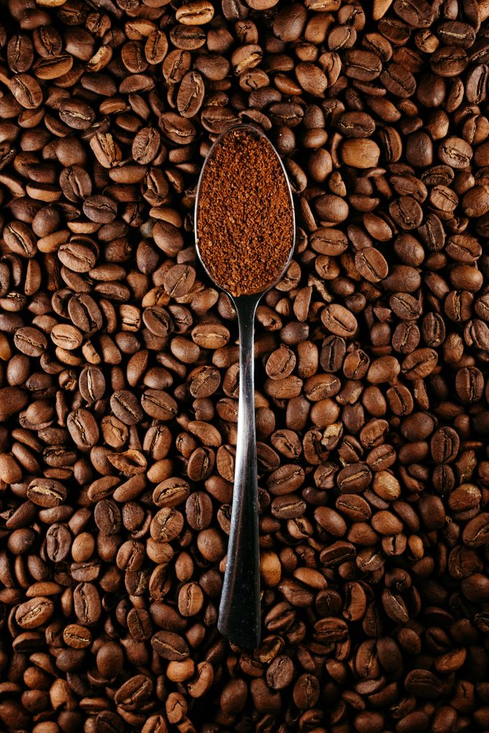 Top view of a spoon with ground coffee on a bed of whole coffee beans.