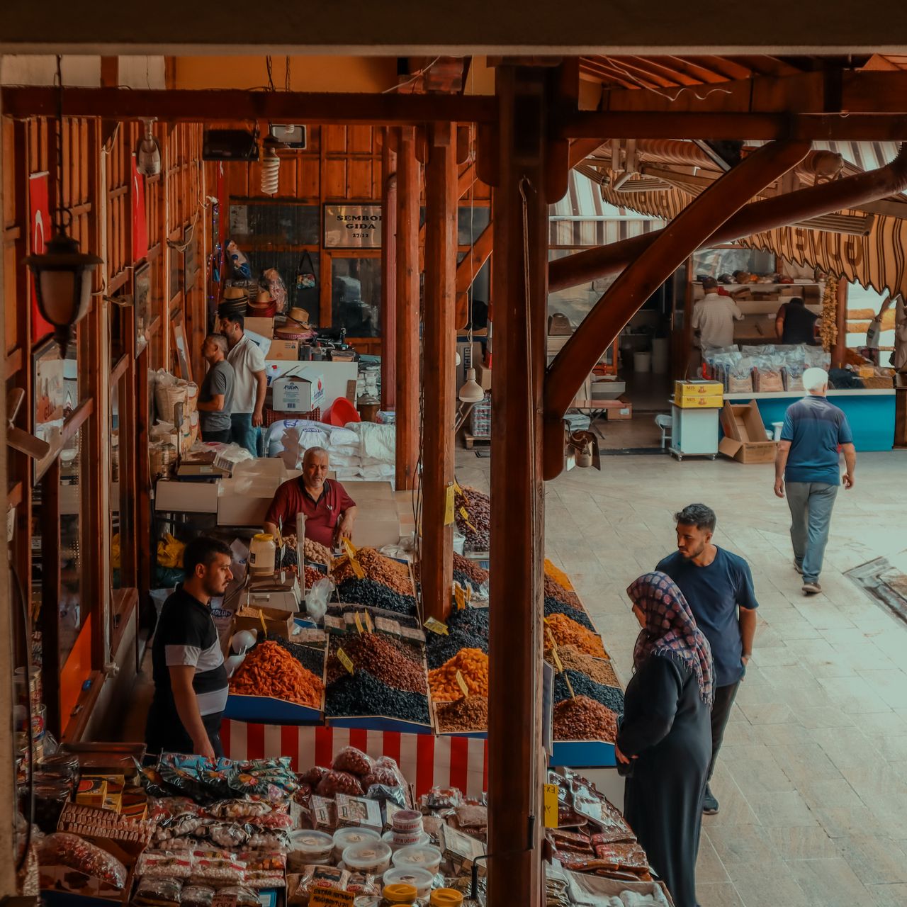 A lively market in Sivas, Türkiye showcasing vendors, dried fruits, and shoppers under a wooden pavilion.