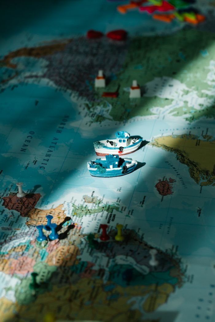 Close-up of toy boats and figurines on a world map, highlighted by a sunbeam.
